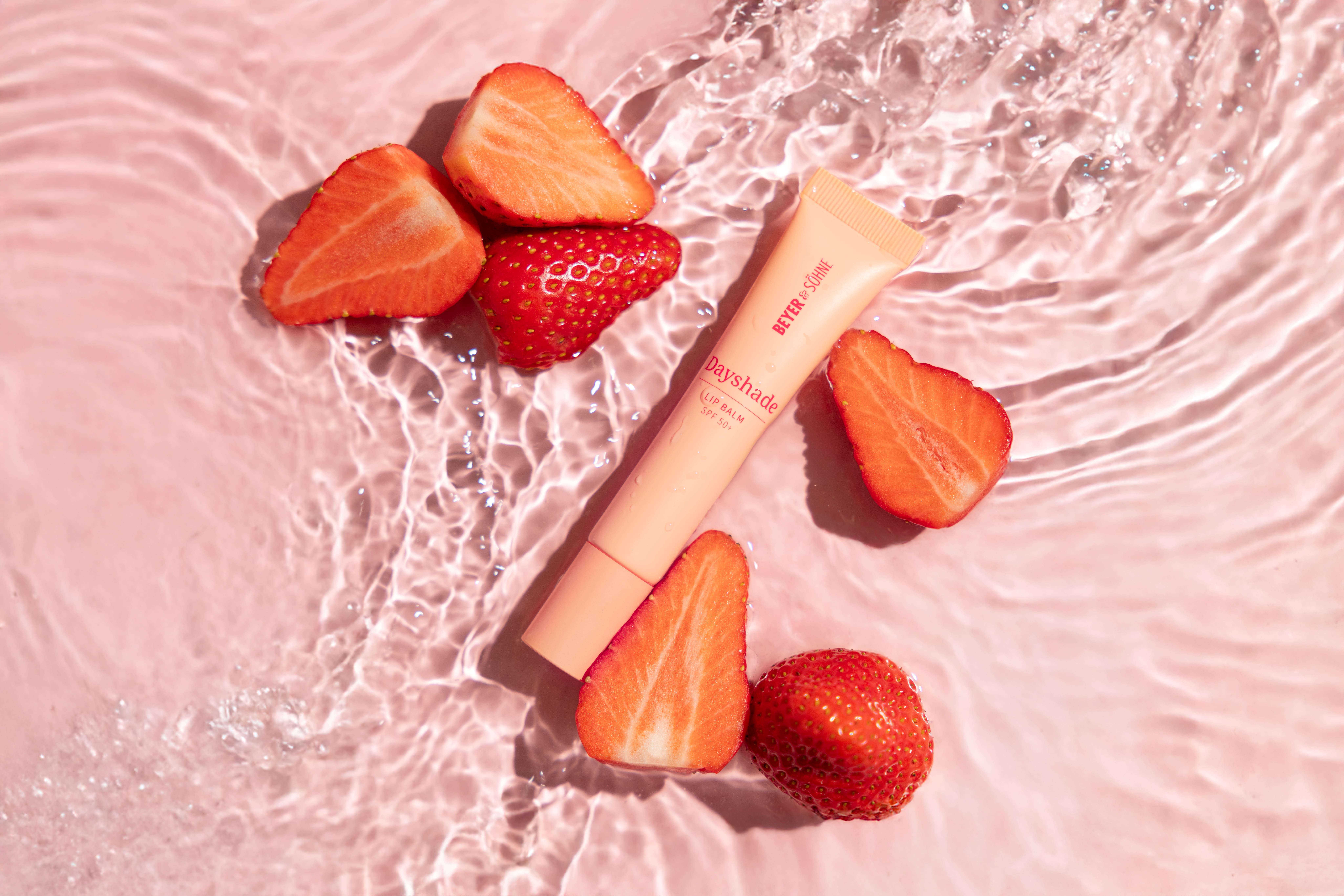 Beyer & Söhne Dayshade Lip Balm mit SPF 50+ auf einer Wasseroberfläche, umgeben von frischen Erdbeeren – inspiriert von der feuchtigkeitsspendenden und schützenden Wirkung natürlicher Inhaltsstoffe.